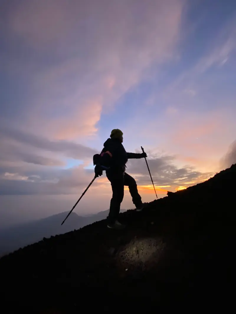 Trekker silhouetted with poles on the ridge as the sun comes up